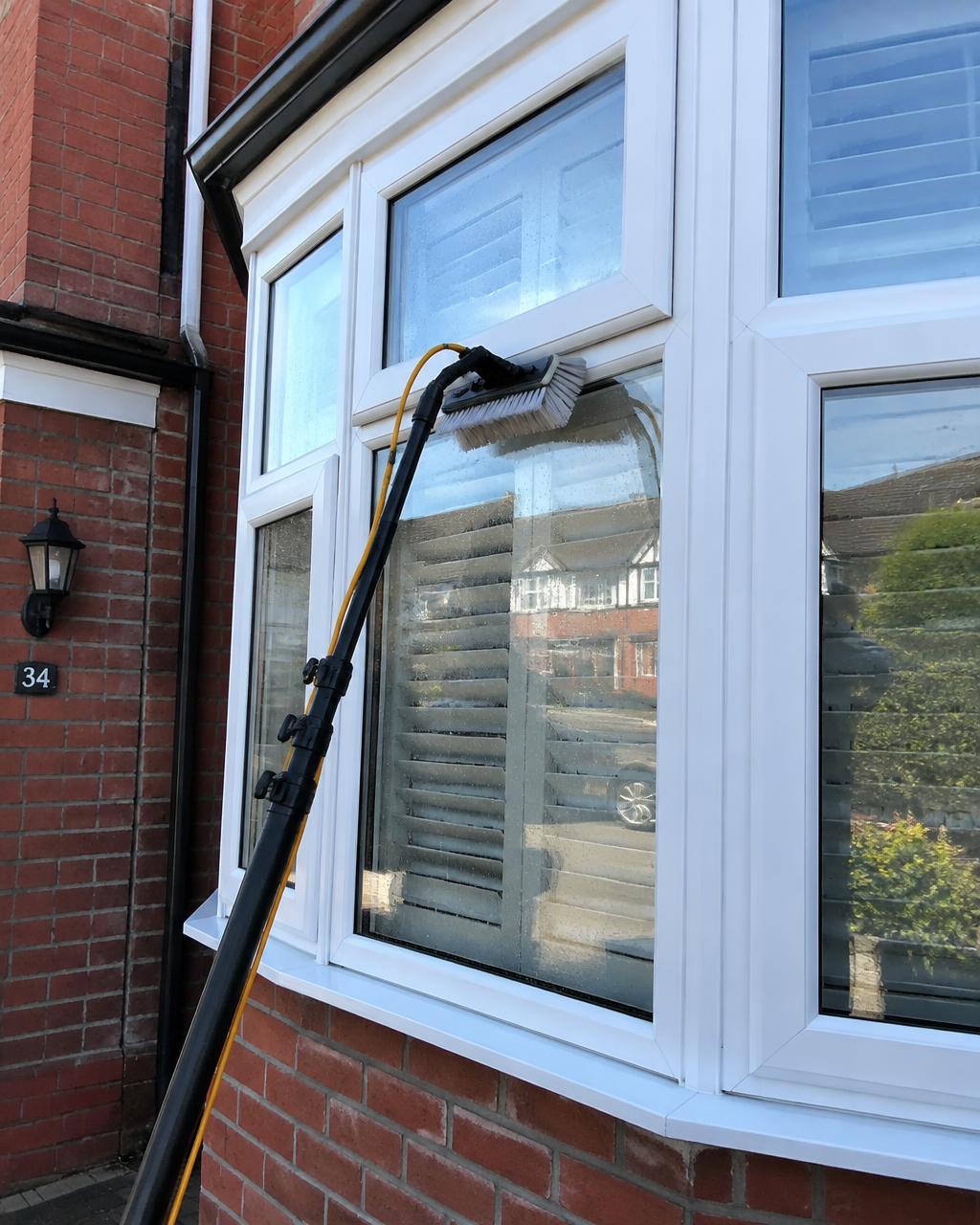 Pure water pole and brush cleaning a white uPVC bay window on a Northampton home